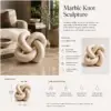 Beige marble knot sculpture styled on a coffee table in a luxury living room setting.